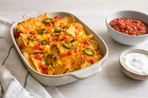 Chipsy tortilla zapieczone roztopionym serem z papryką, kukurydzą i jalapeño w foremce, obok salsa