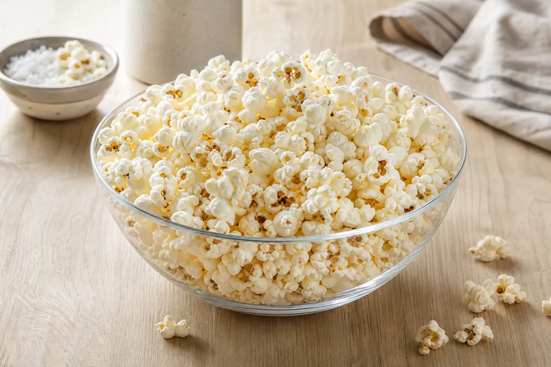 Biały puszysty popcorn w dużej szklanej misce, posypany solą, na drewnianym stole