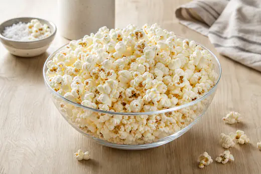 Biały puszysty popcorn w dużej szklanej misce, posypany solą, na drewnianym stole