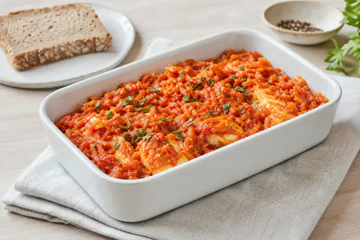 Kawałki dorsza w mące ułożone na gęstej pomidorowej sauté z marchewki, pietruszki i selera na półmisku