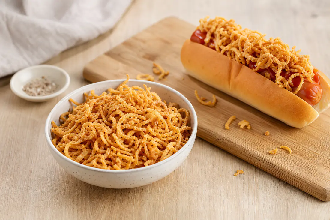 Miska złotej, chrupiącej prażonej cebulki obok hot doga posypanego cebulką na drewnianej desce