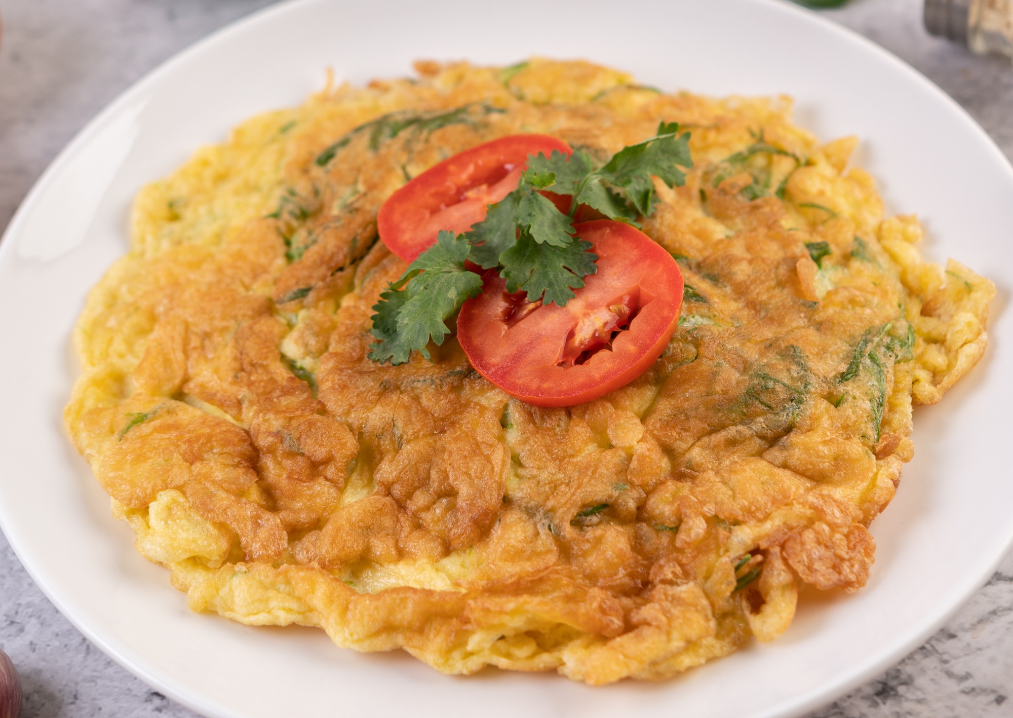 Omlet w frytkownicy beztłuszczowej podany na białym talerzu z dodatkiem świeżych warzyw.